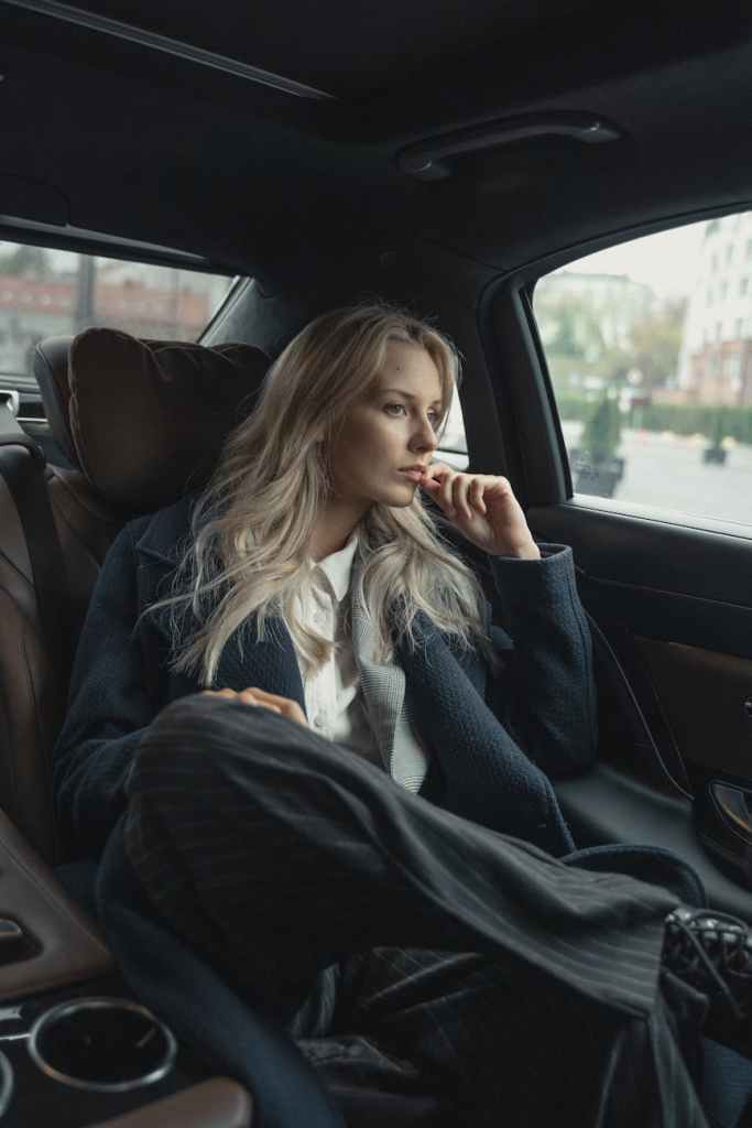 “Woman in black suit sitting in car, reflecting on success and faith.”